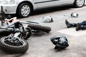 A motorcyclist, a helmet, and motorcycle on the ground after a car accident.